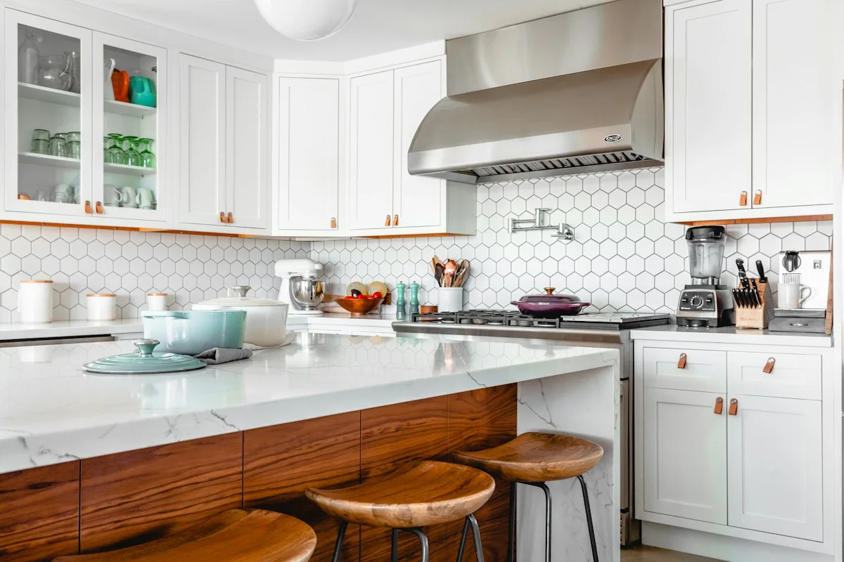 Bright white kitchen with island, wooden stools and pale blue cookware