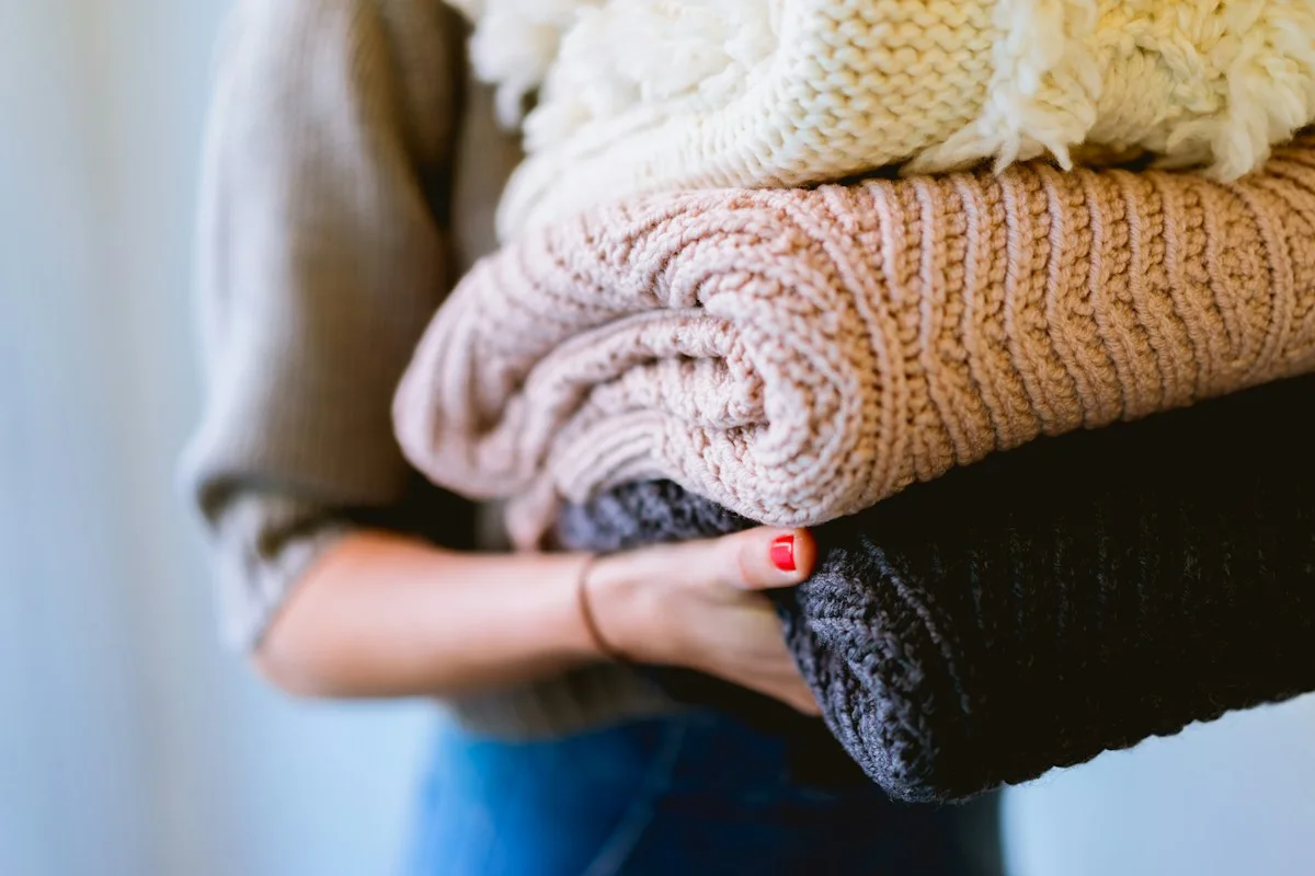 Person holding a stack of folded knitted garments
