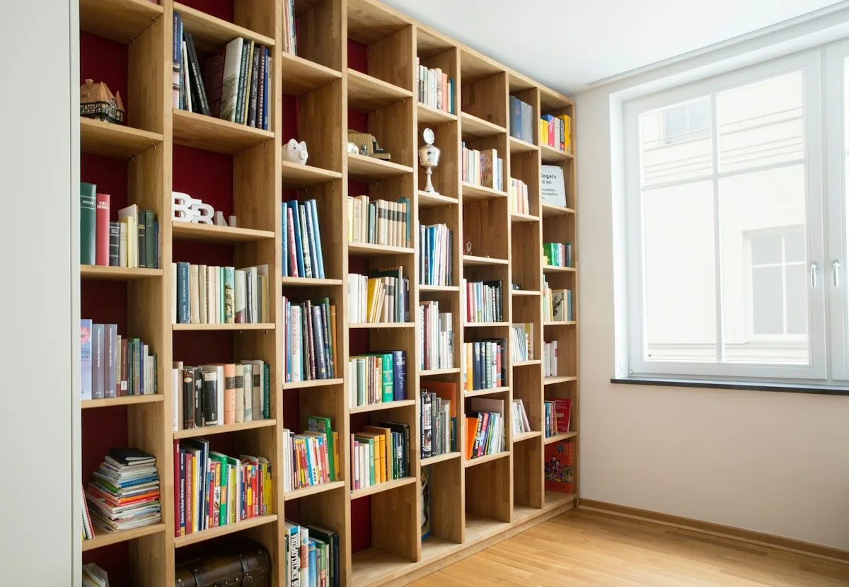 Tall wooden bookcases filled with books beside a bright window